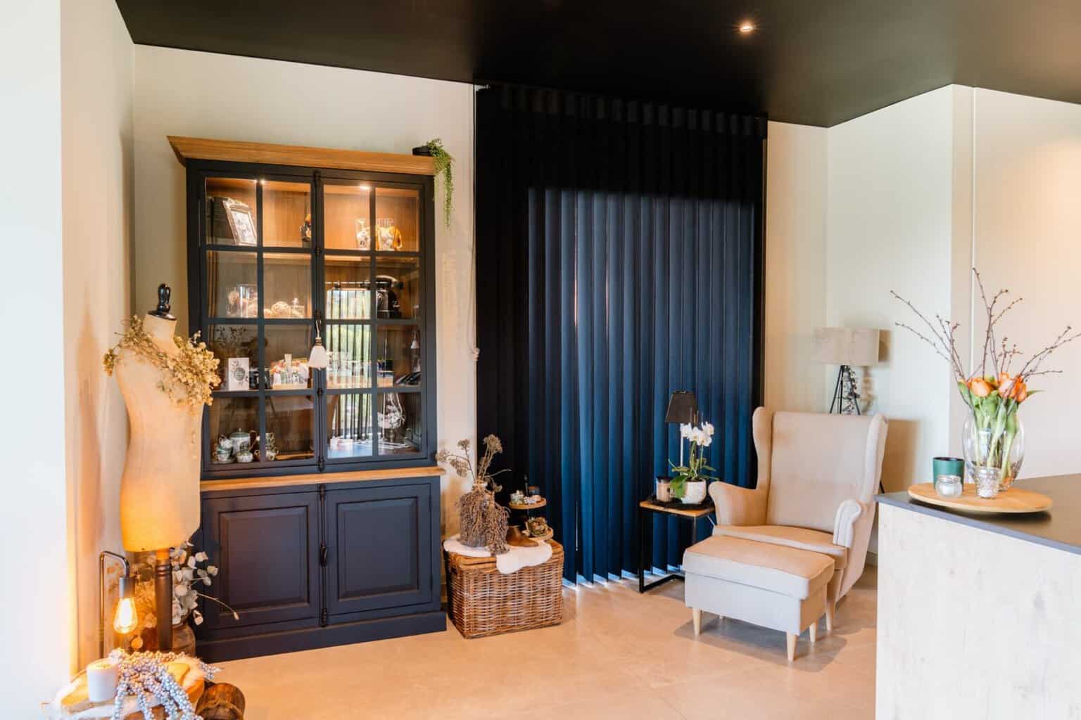 Zwarte Illusions verticale lamellen gesloten naast vitrinekast en lichte fauteuil met voetenbank — woning Luyten BalenZwarte Illusions verticale lamellen gesloten naast vitrinekast en lichte fauteuil met voetenbank — woning Luyten Balen