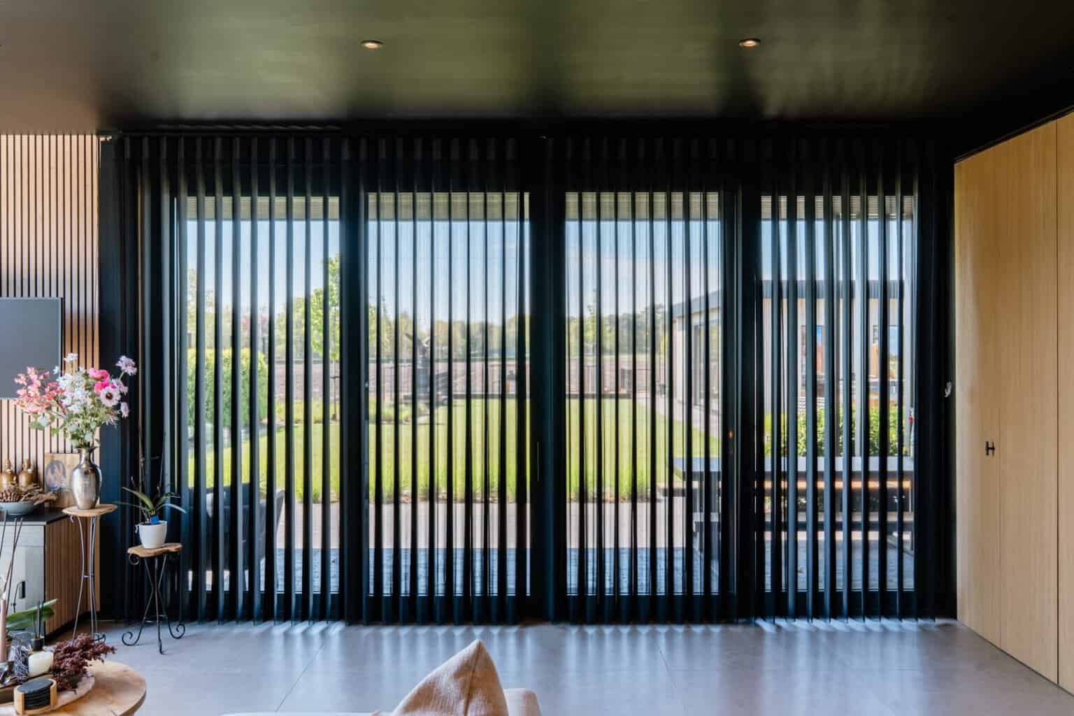 Volledig zicht op zwarte Illusions lamellen langs brede raamwand met tuinzicht — Balen