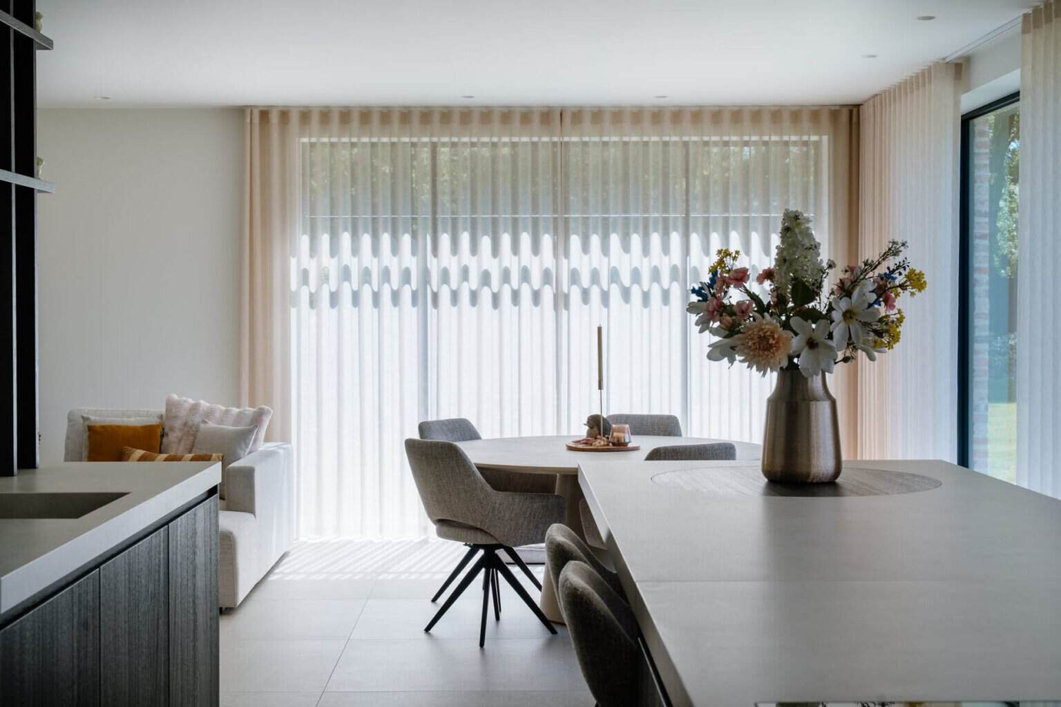 Doorzicht vanuit keuken naar eetplaats en living met wave vitrage - open leefruimte woning Balen