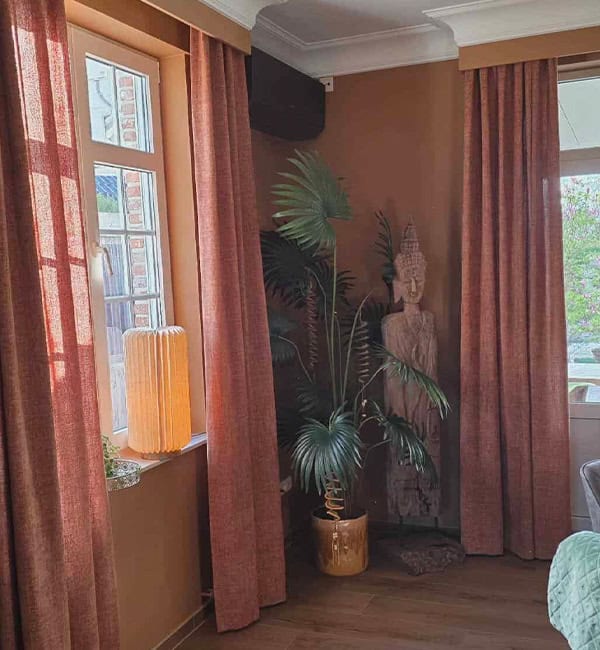Roestbruine chenille gordijnen in boho woonkamer met sierlijst en Boeddha wanddecoratie – sfeervolle gordijnen van Aerts Interieur Lommel