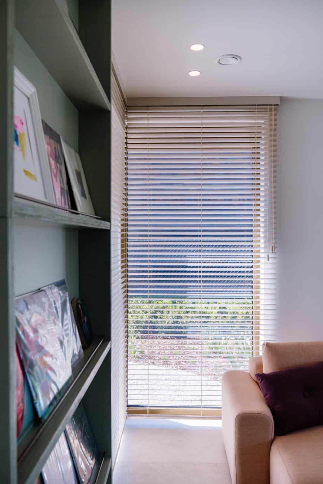 Detail houten lamellen met lichtspel naast boekenkast — living woning Lommel