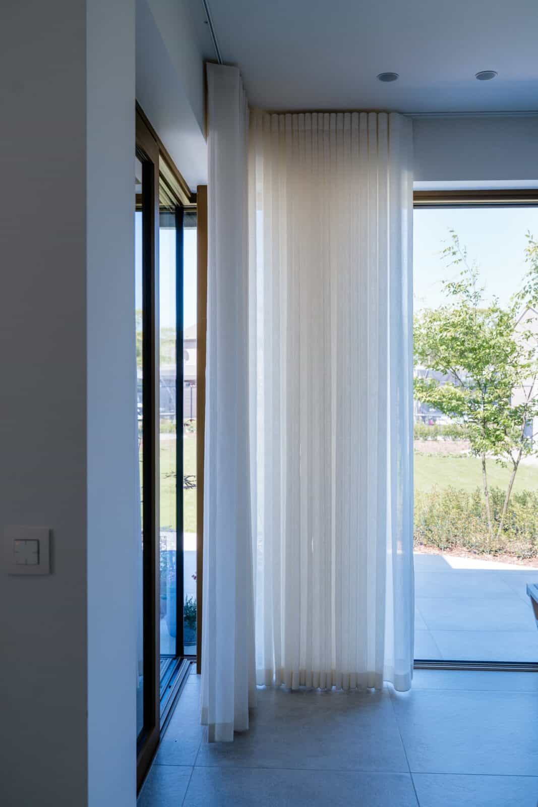 Transparant wave gordijn langs grote raampartij met tuinzicht — inkomhal woning Lommel