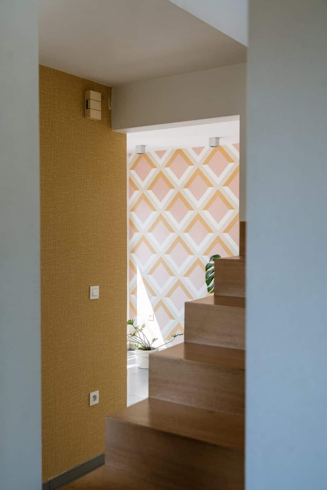 Geometrisch ruitpatroon behang naast trap met houten treden — gang woning Mol