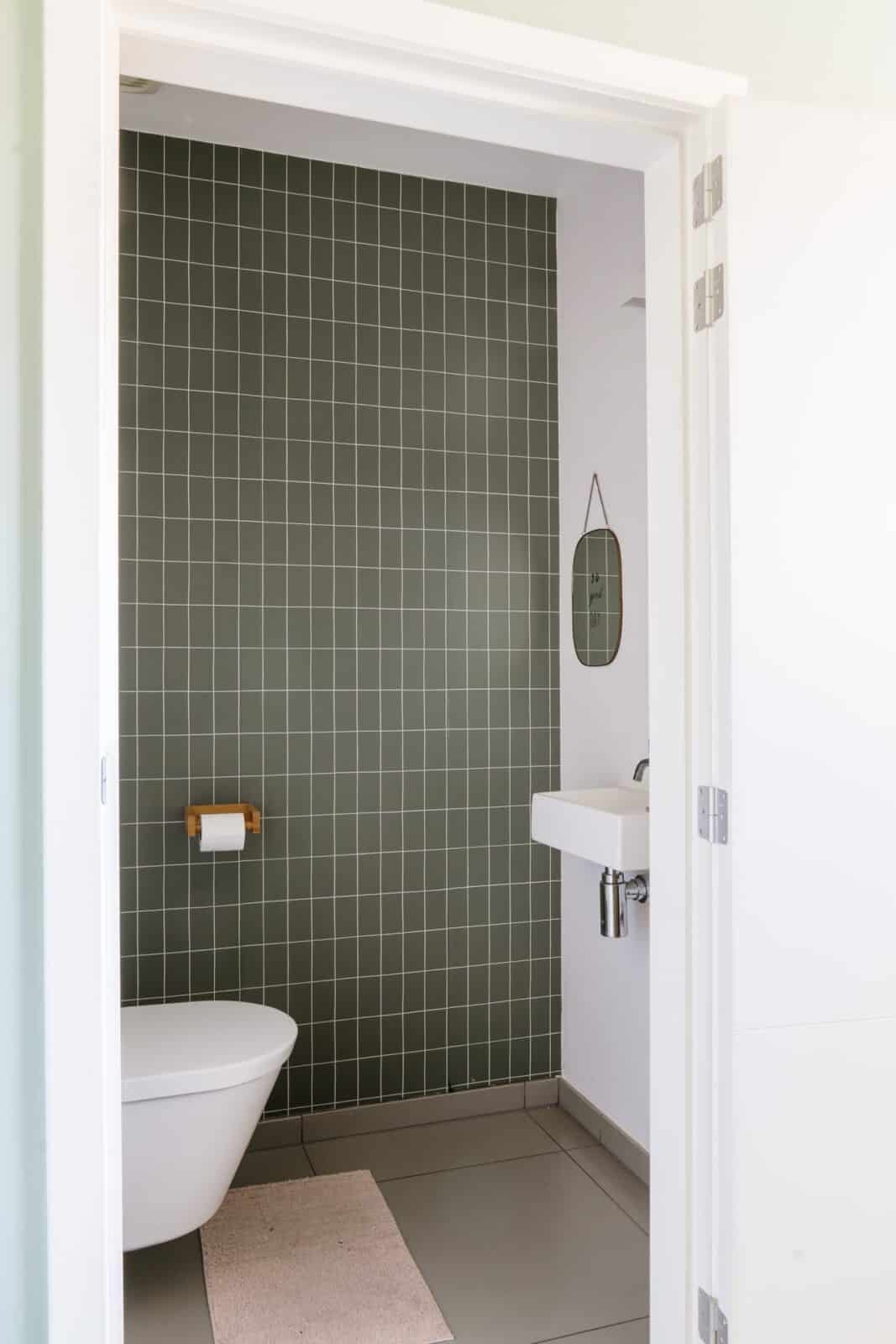 Overzicht gastentoilet met donkergroen tegelbehang en wandspiegel — woning Lodewijcks