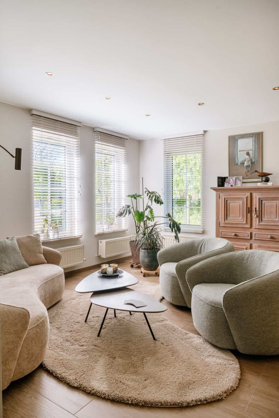 Overzicht living met witte houten lamellen, rond tapijt en groene fauteuils — woning Pelt