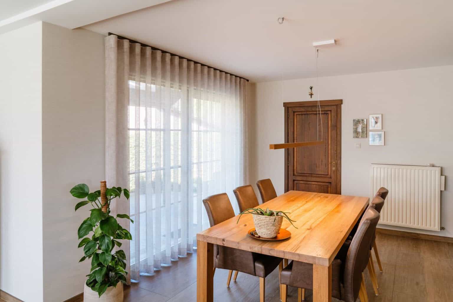 Wave gordijn langs volledige raamwand in eetkamer met houten tafel — woning Pelt