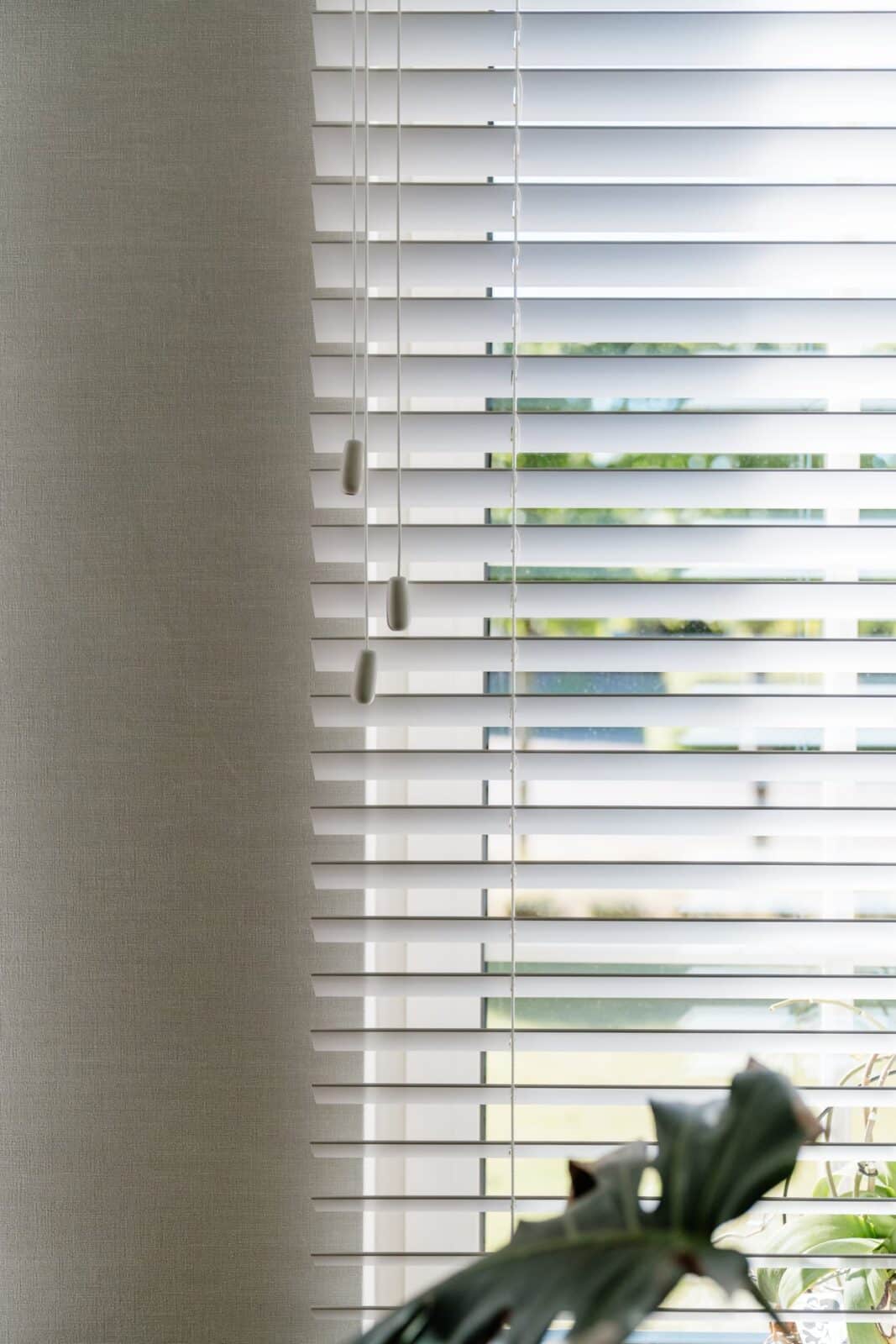 Detail witte houten lamellen naast wave gordijn met lichtinval — woning Pelt