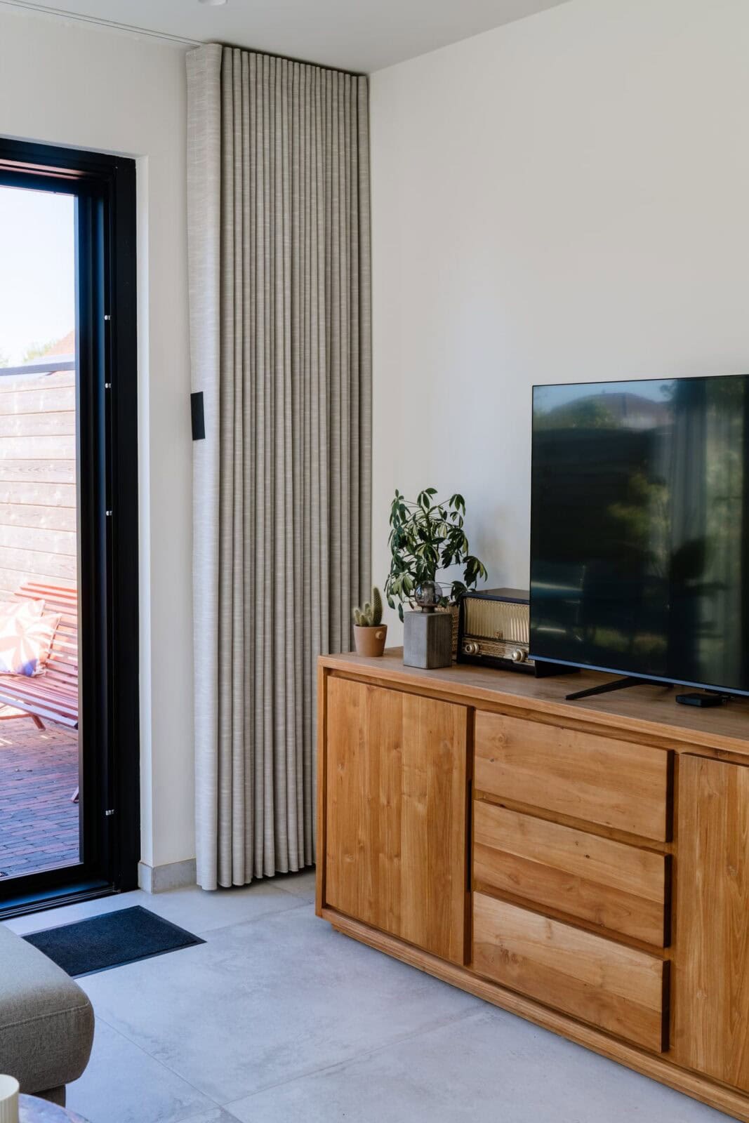 Wave gordijn naast terrasdeur met houten tv-meubel en kamerplant — woning Lommel
