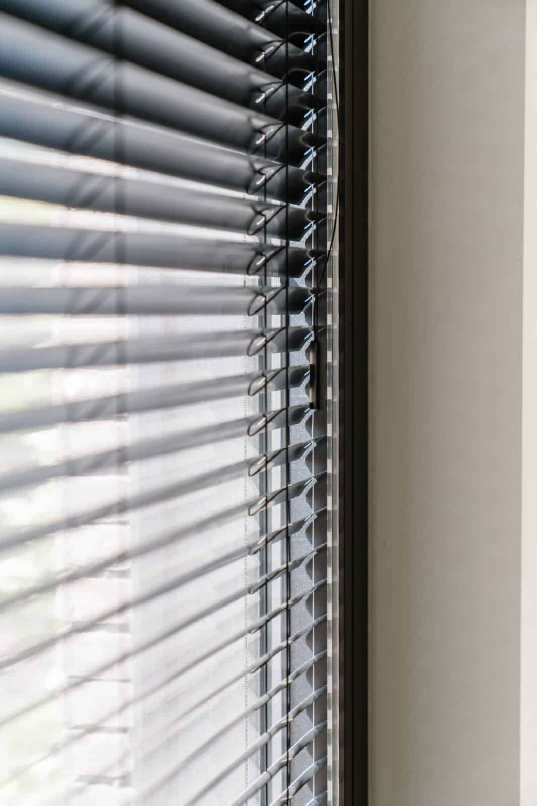 Close-up antraciet aluminium lamellen met lichtinval — woning Lommel