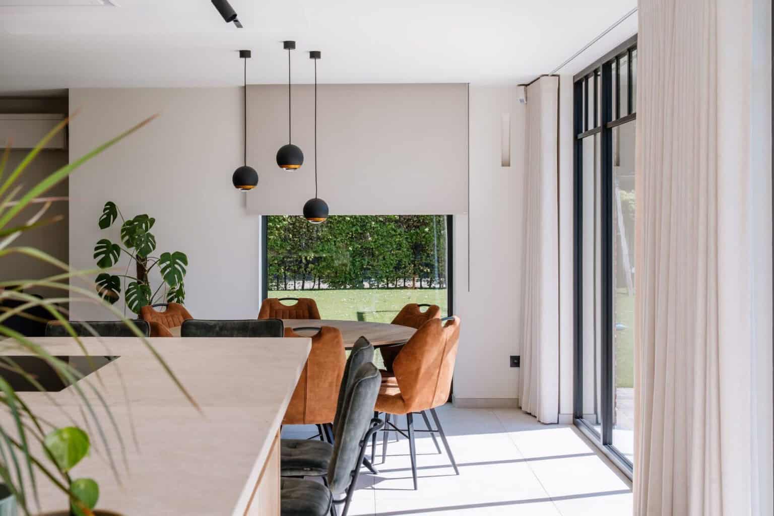 Doorzicht vanuit keuken naar eetruimte met wave gordijnen langs stalen ramen - open leefruimte woning Retie