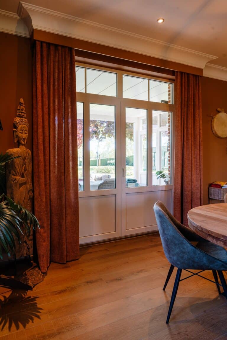 Roestbruine gordijnen voor tuindeur met boeddhabeeld en ronde tafel - eetruimte woning Lommel
