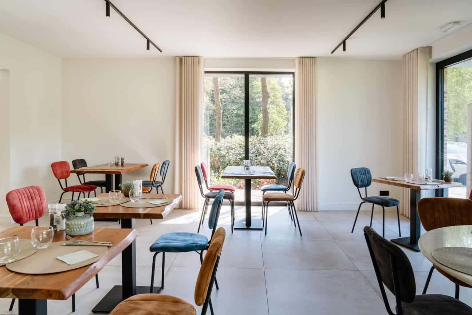 Ontbijthoek met wave gordijnen, houten tafels en kleurrijke stoelen — boetiekhotel Lommel