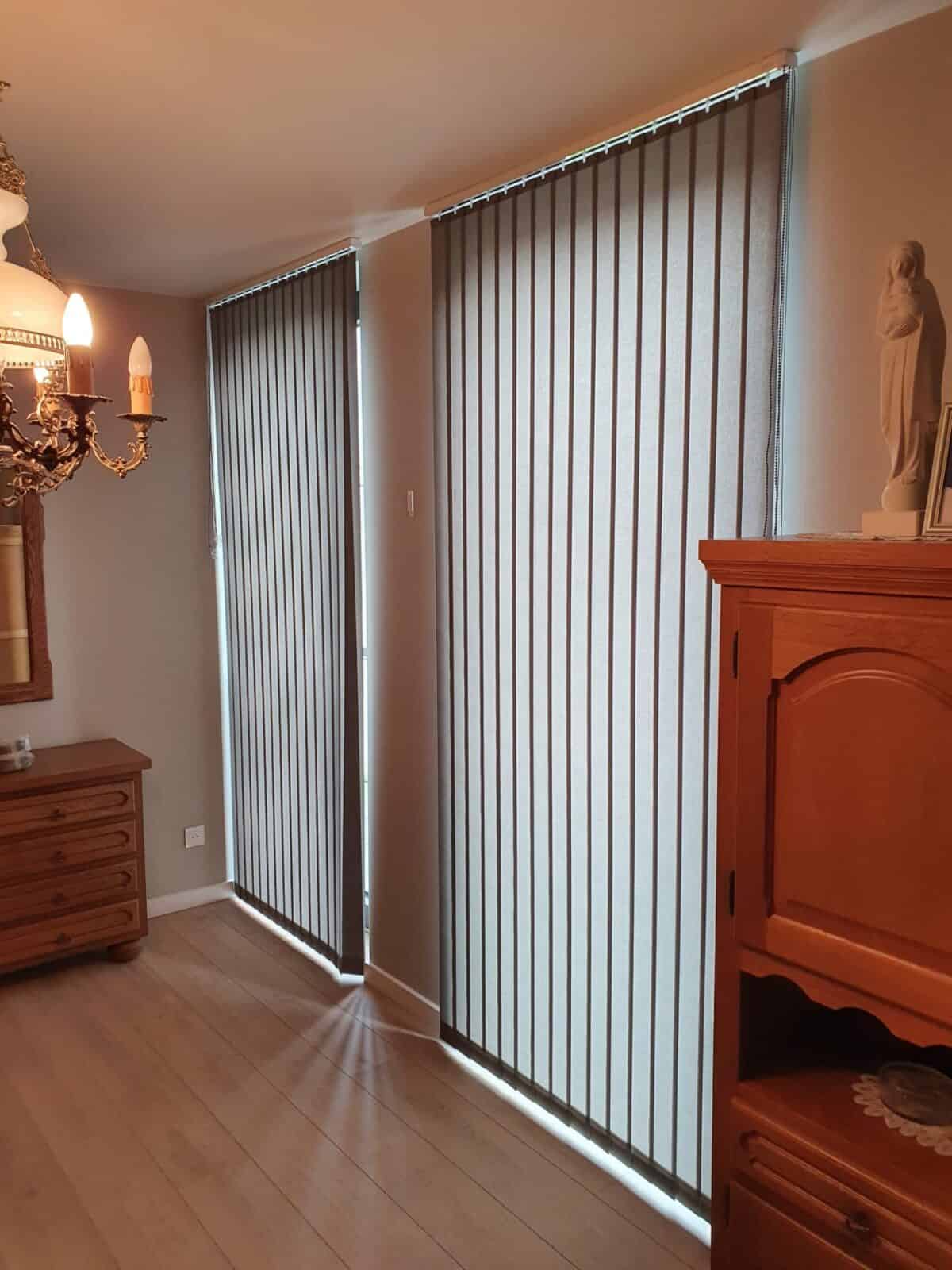 verticale lamellen aan twee grote ramen in een klassieke kamer met houten meubels en kandelaber – realisatie Aerts Interieur Lommel