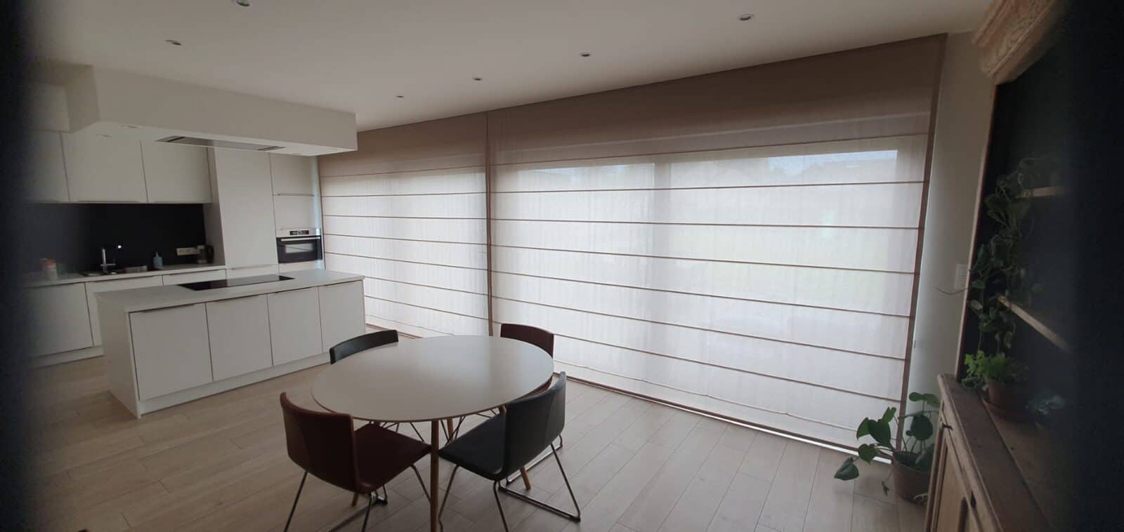 Grote vouwgordijnen in beige linnen stof over volledige glazen wand in open leefkeuken – op maat geplaatst door Aerts Interieur Lommel
