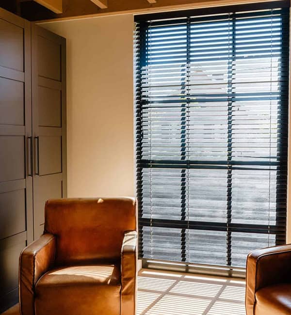 Donkere houten lamellen voor groot raam met lederen fauteuils en balkplafond - zithoek boven woning Geel - cropped